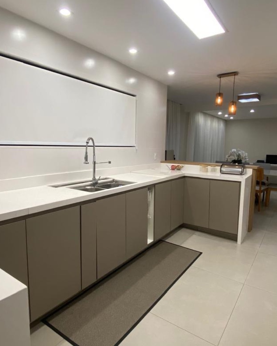 Cozinha em L com marcenaria clara, bancada branca, pendentes e iluminação embutida
