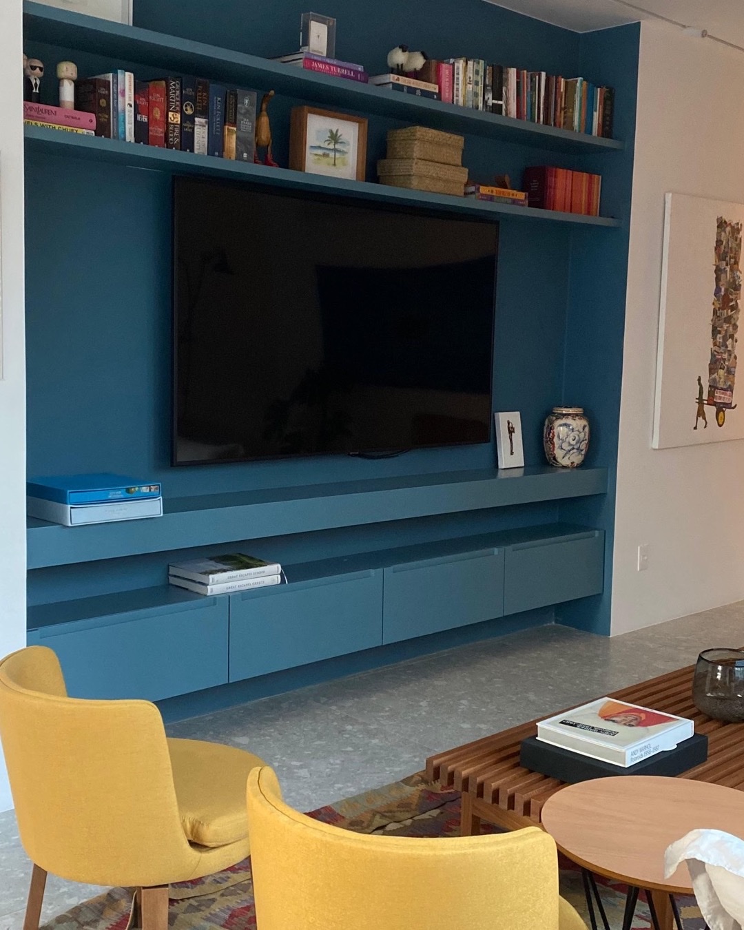 Estante azul sob medida com TV embutida, poltronas amarelas e mesa de centro ripada