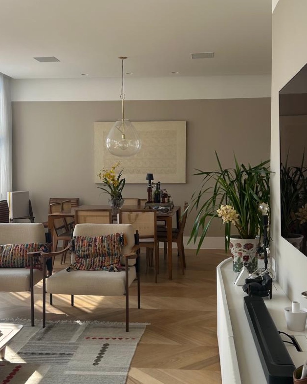 Sala integrada com piso de madeira em espinha de peixe, mesa de jantar e cadeiras de palha