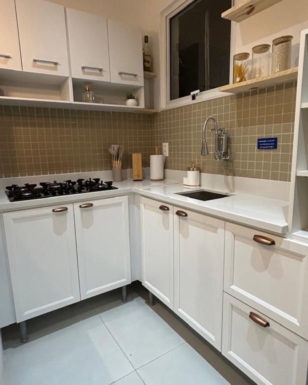 Cozinha em L com marcenaria branca, azulejo verde-oliva e puxadores em cobre
