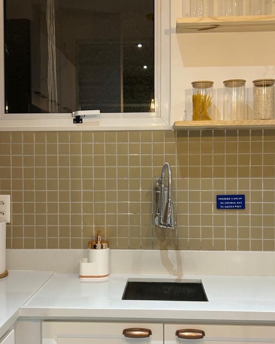 Detalhe de cozinha com bancada branca, cuba embutida, azulejo verde-oliva e prateleira de madeira