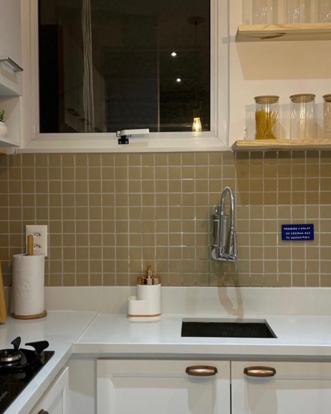 Cozinha com azulejo verde-oliva, bancada branca, prateleira de madeira e cuba embutida