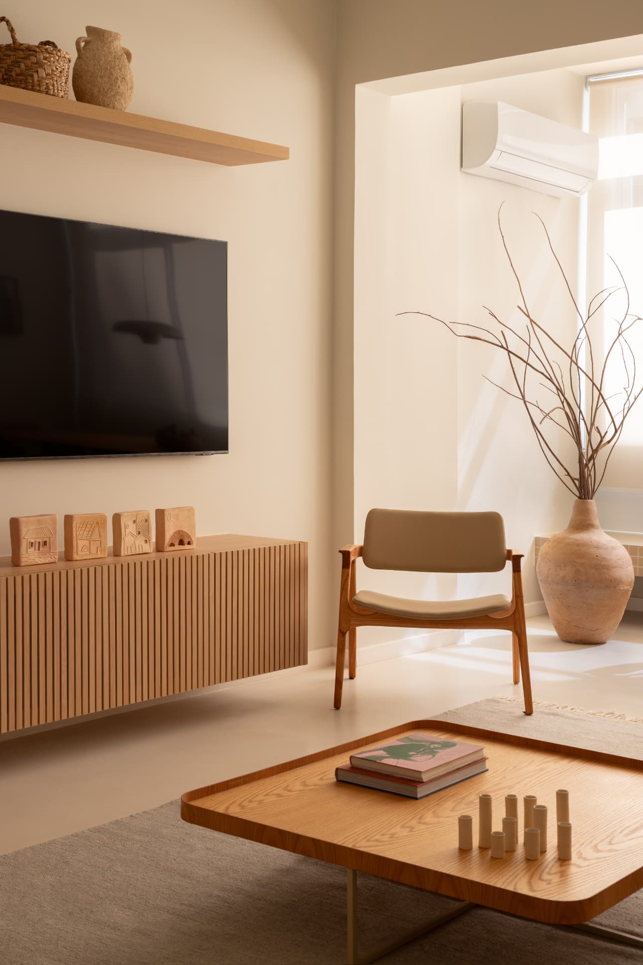 Sala de TV com rack ripado suspenso, prateleira de madeira, poltrona de braços e vaso de cerâmica junto à janela