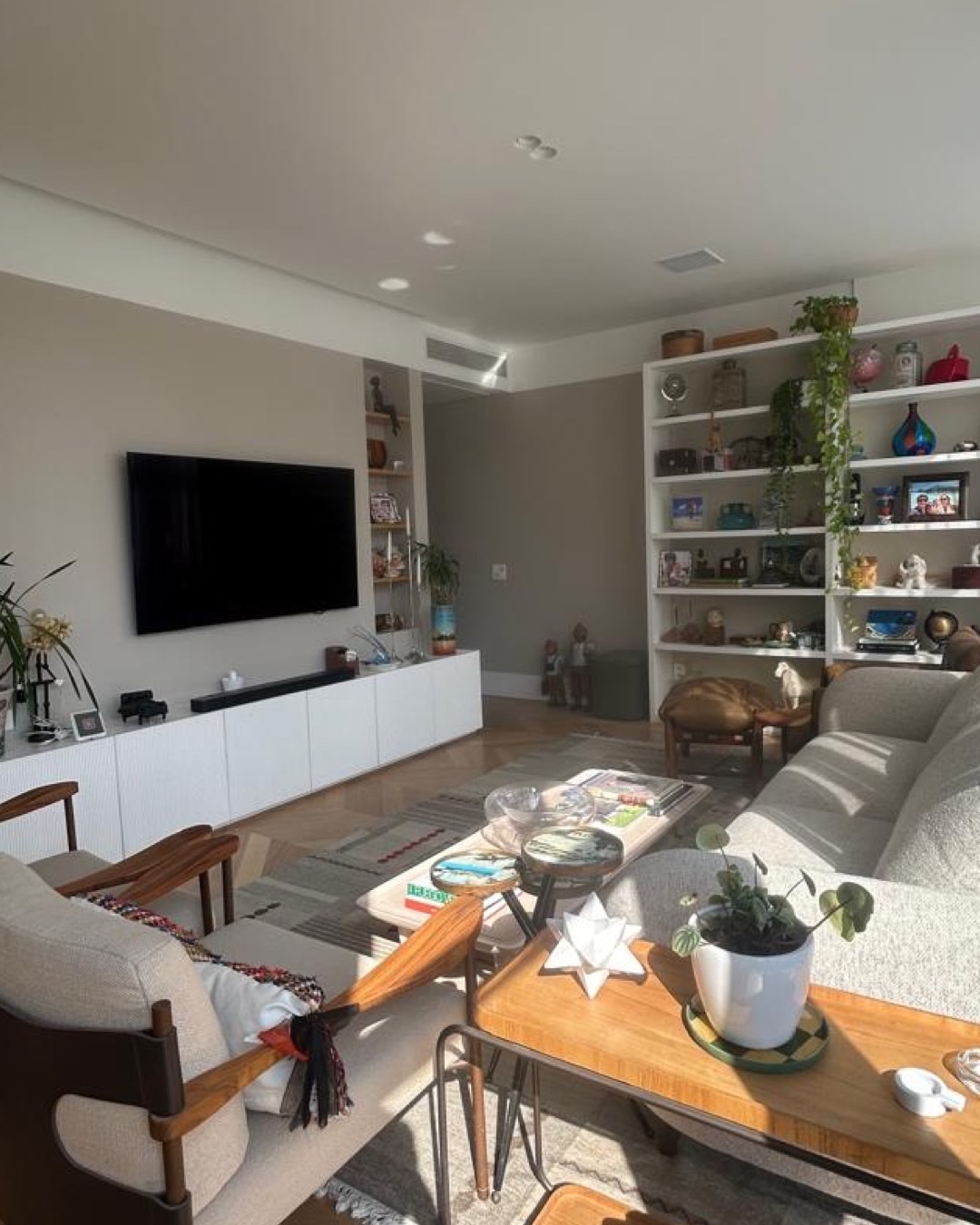 Sala de TV com painel branco, estante com nichos decorados e sofá cinza claro