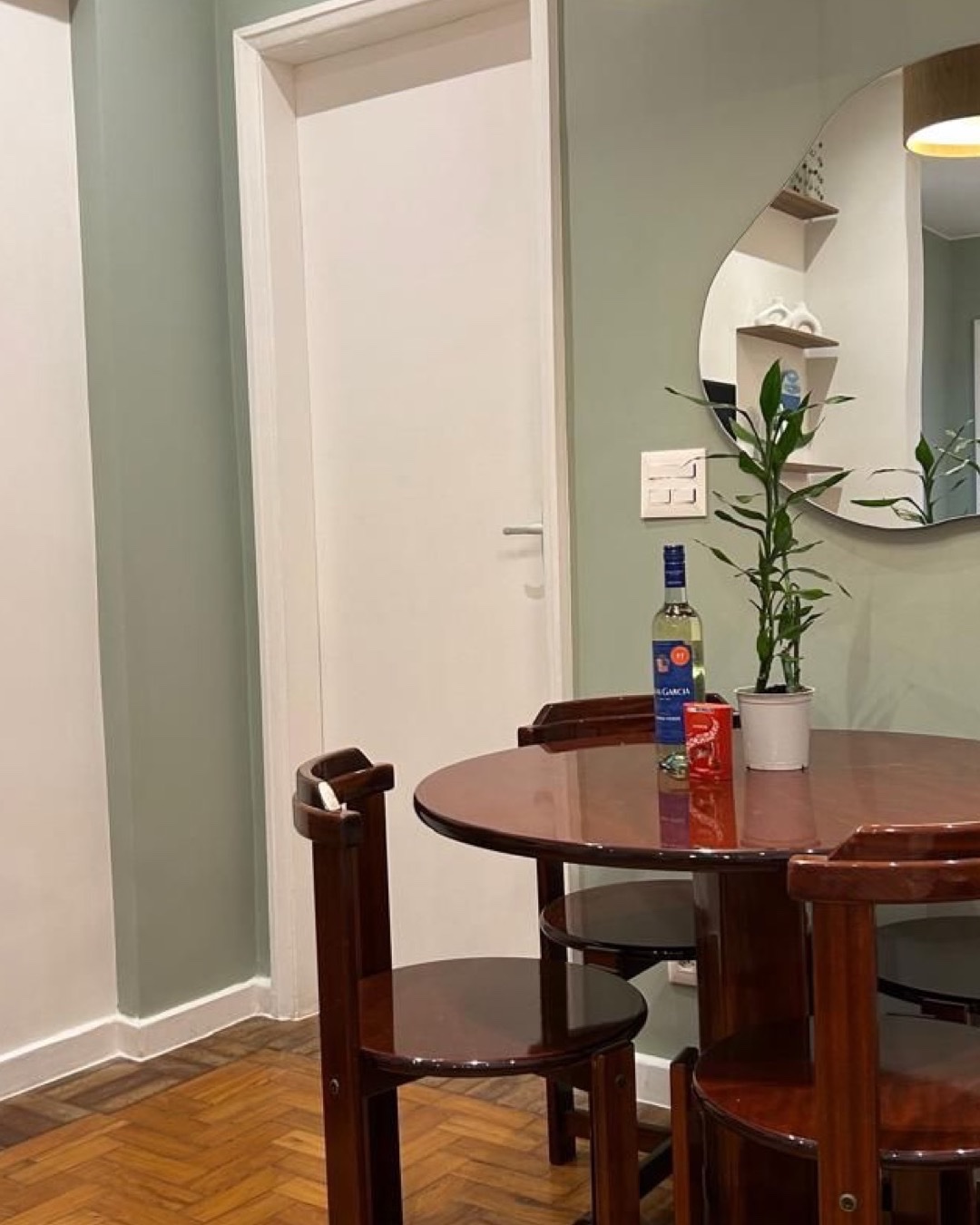 Sala de jantar com parede verde, mesa redonda de madeira escura e espelho orgânico
