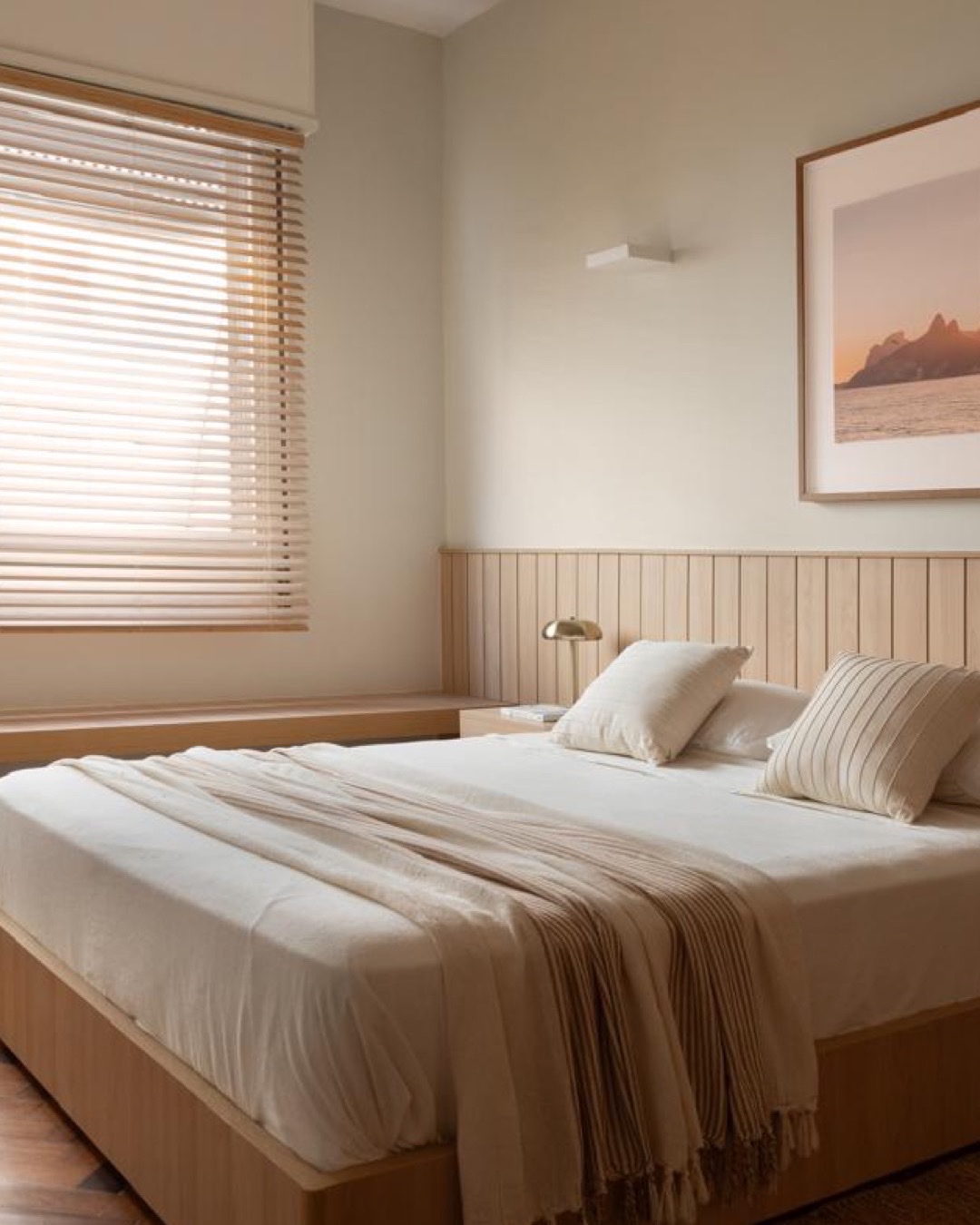 Dormitório com cabeceira ripada em madeira, cama com roupa neutra e persiana de madeira