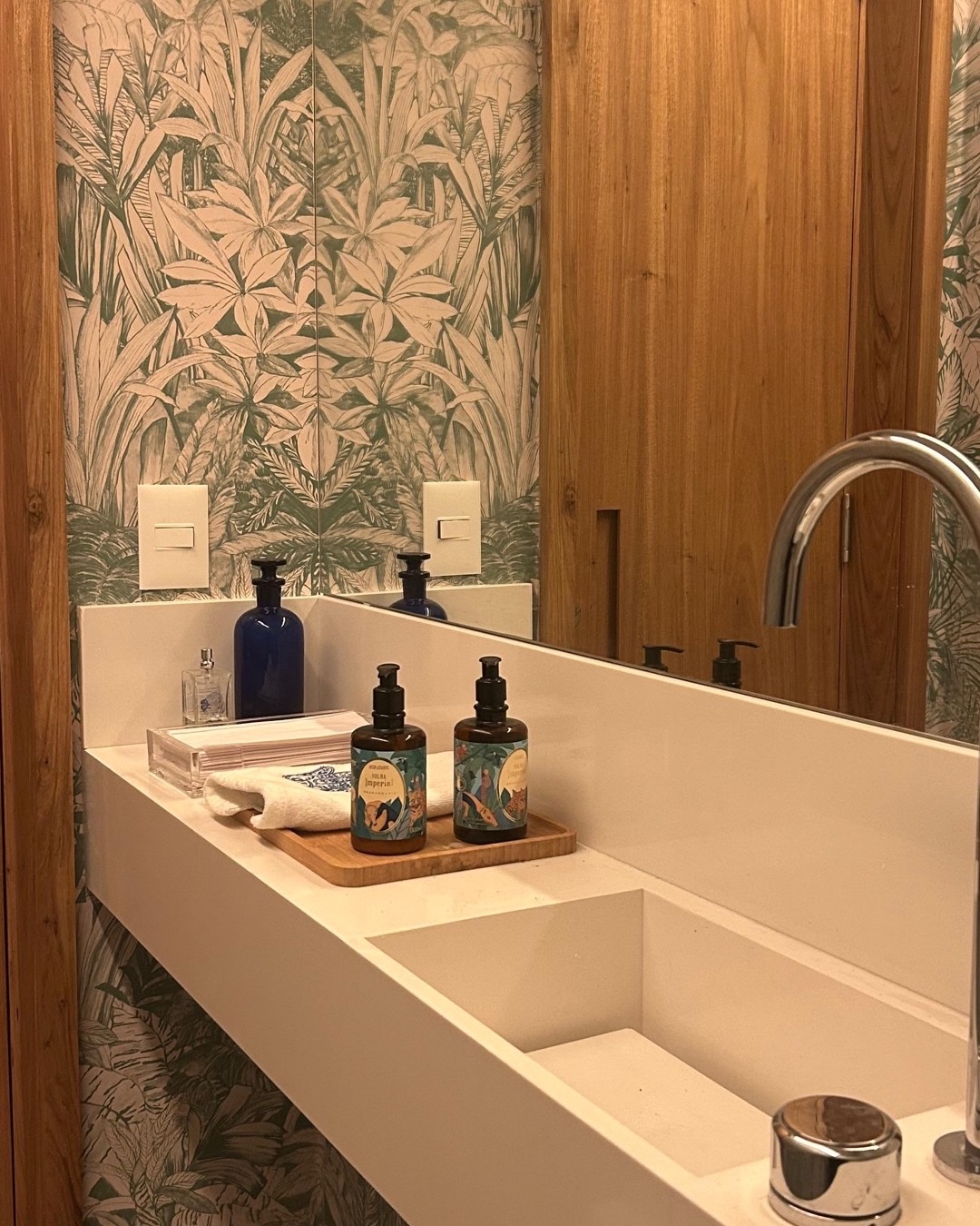 Lavabo com papel de parede botânico, porta de madeira e cuba branca esculpida