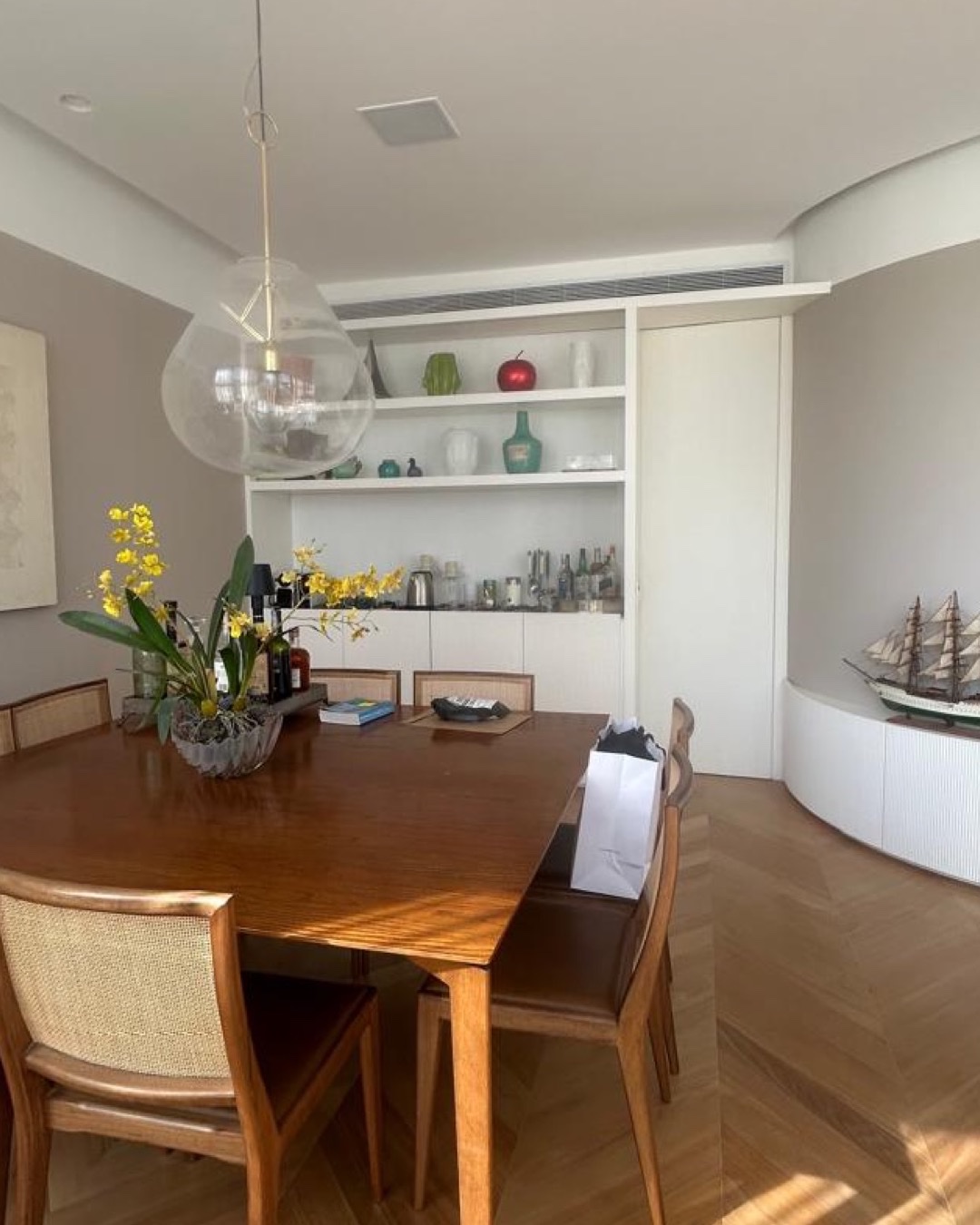 Sala de jantar com mesa de madeira, pendente de vidro e marcenaria branca com bar