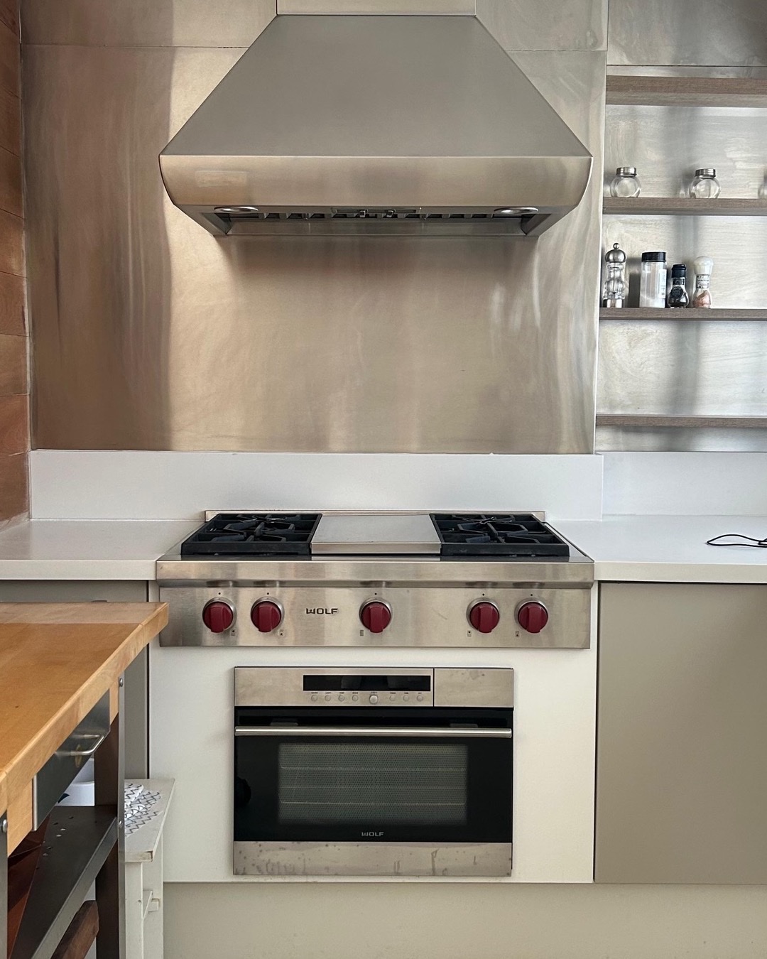 Cozinha com fogão e revestimento em inox, coifa e bancada de madeira