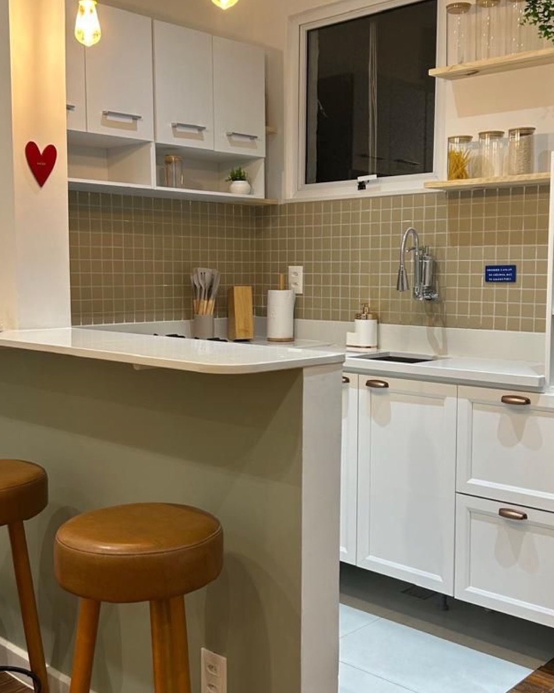 Cozinha com bancada bar em pedra branca, azulejo verde-oliva, marcenaria branca e banquetas de couro